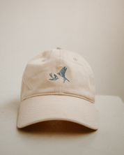 Beige cap with a small embroidered blue swallows design on a light beige background