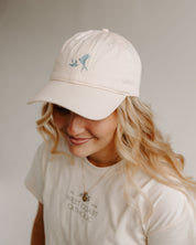 Woman wearing a beige cap with blue swallows and t-shirt with text on a plain background