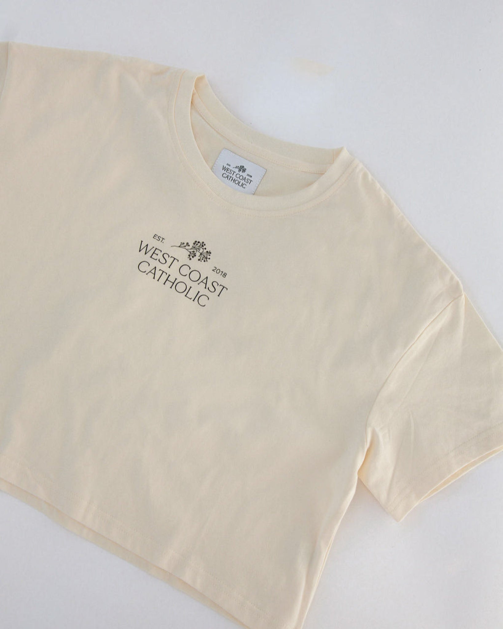 Cream t-shirt with 'West Coast Catholic' text on a white background