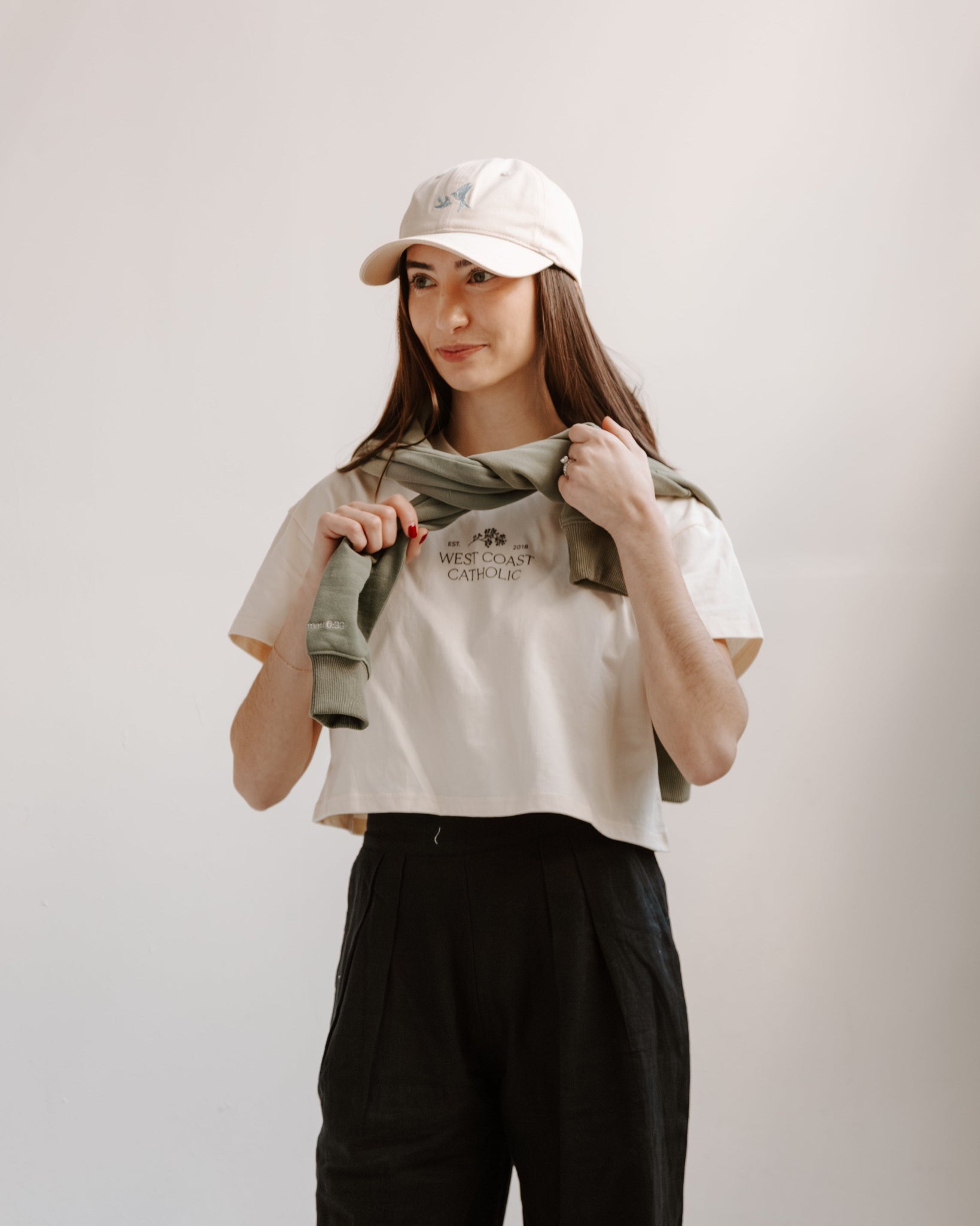 Woman wearing a white cap, white t-shirt with text, and black pants against a plain background
