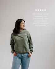 Woman wearing a green sweatshirt with text rating it as one of the softest ever owned.