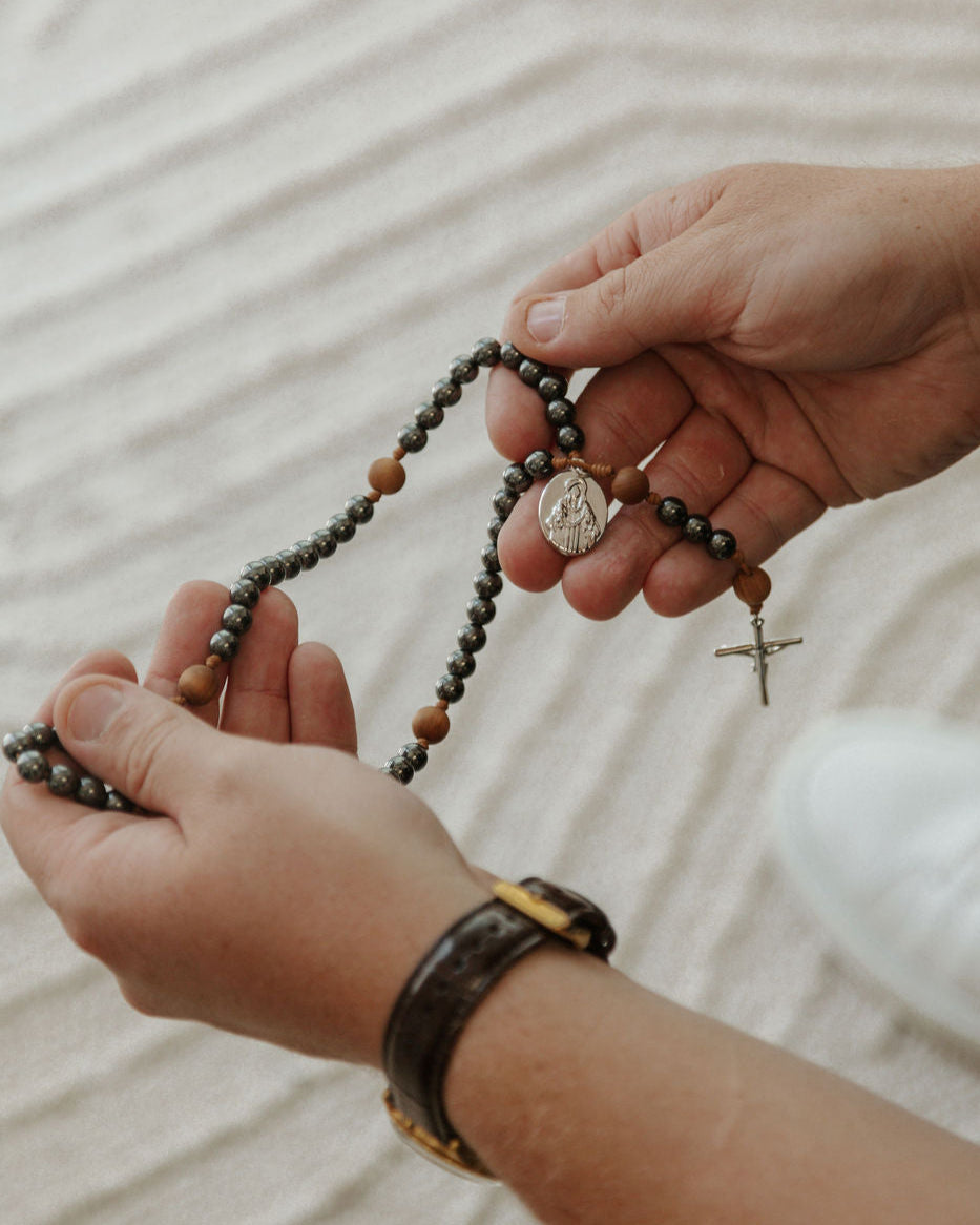 Close-up of hands holding a rosary on a textured fabric background