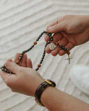 Close-up of hands holding a rosary on a textured fabric background