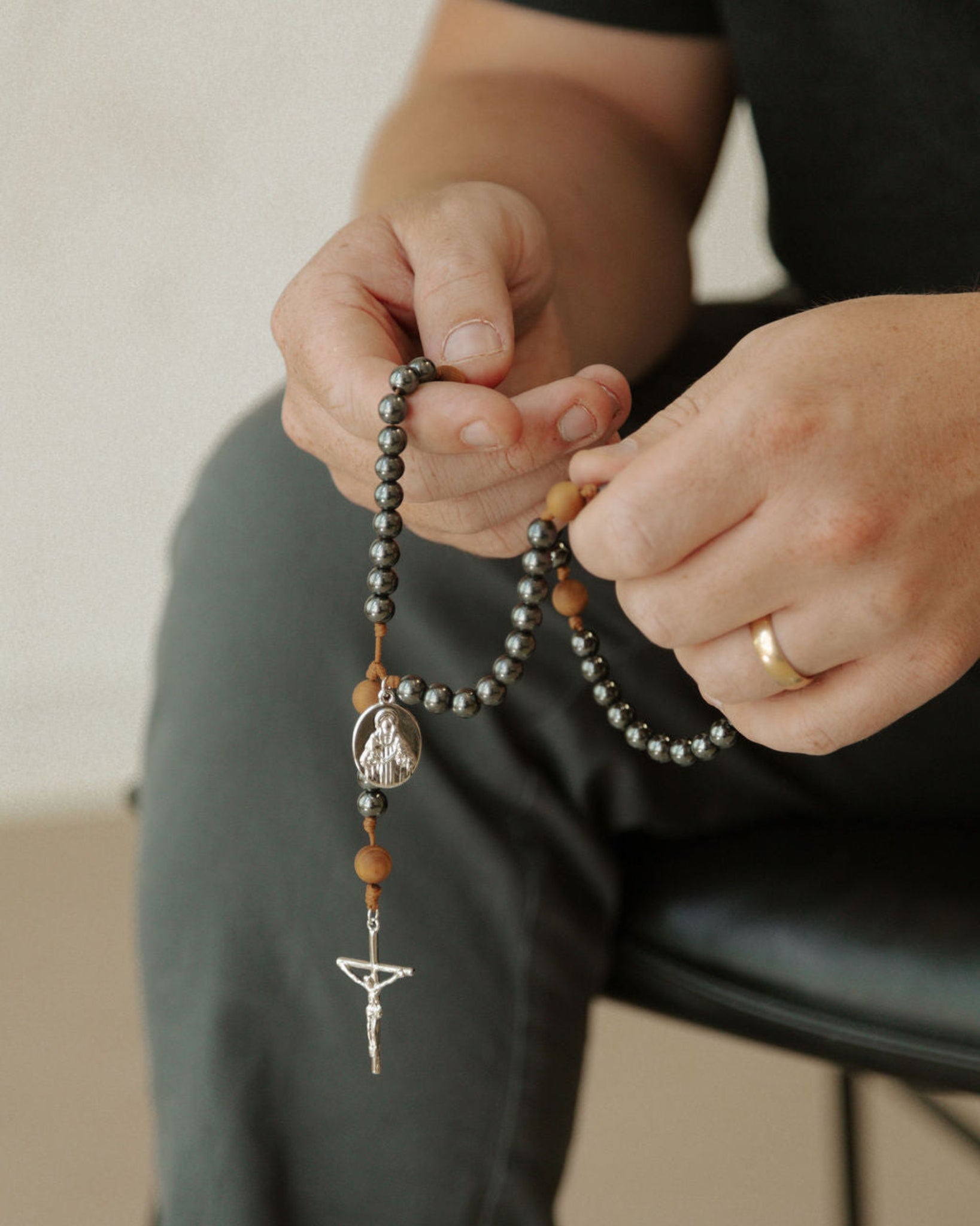Person holding a rosary with a neutral background