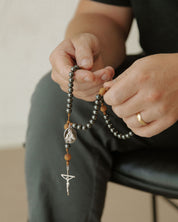Person holding a rosary with a neutral background