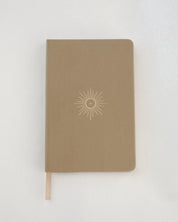 Brown notebook with linen cover and a eucharist emblem embossed on a white background