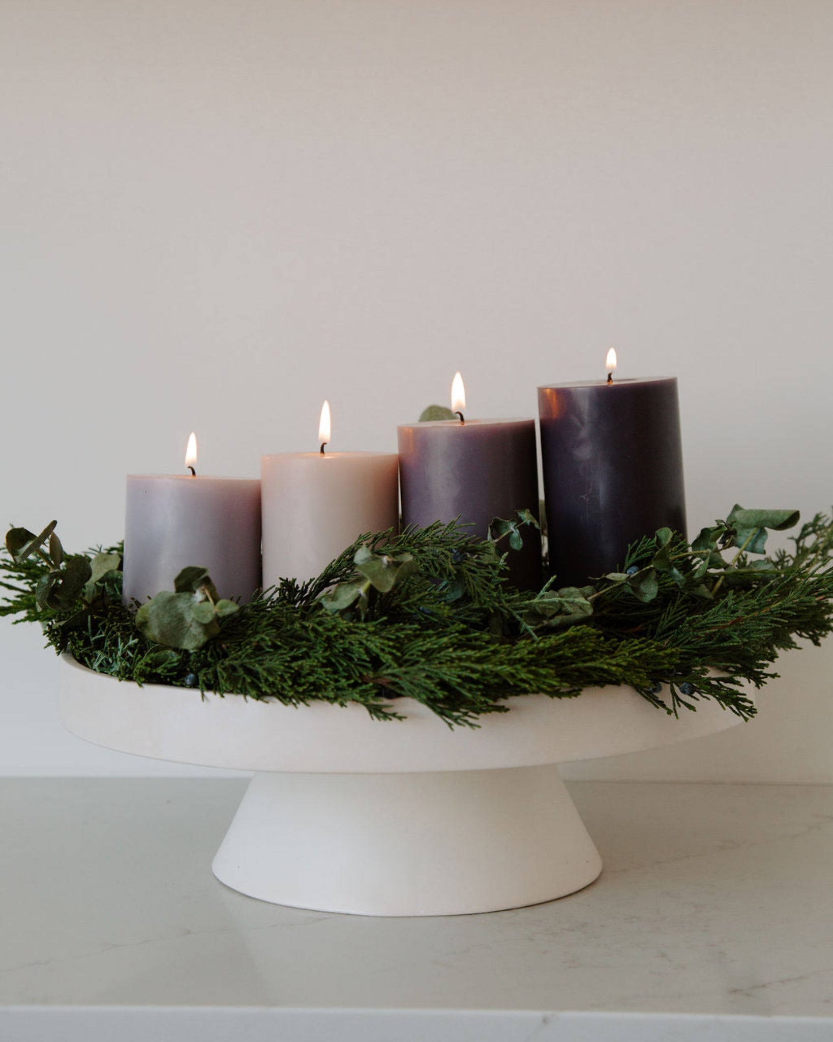 Decorative modern advent wreath with purple candles and greenery on a white stand against a plain background