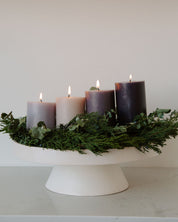 Decorative modern advent wreath with purple candles and greenery on a white stand against a plain background