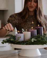 Woman lighting advent candles on a decorative stand with greenery