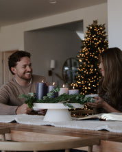 Two people sitting at a table with a advent wreath and decorated Christmas tree in the background