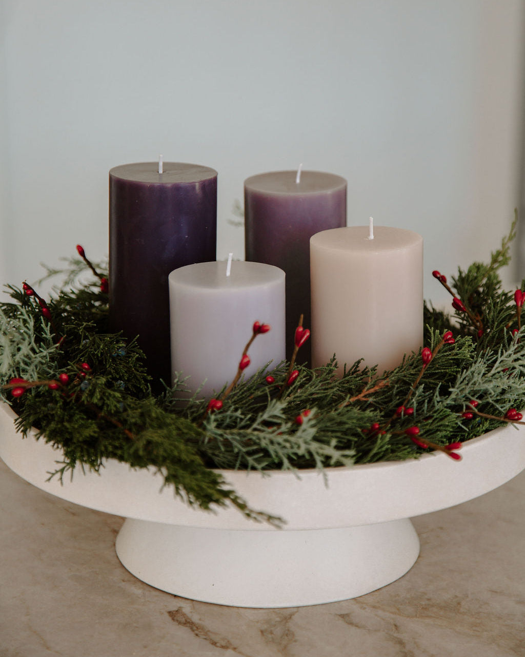 Decorative advent wreath arrangement with purple and white candles on a stand with greenery and red berries.