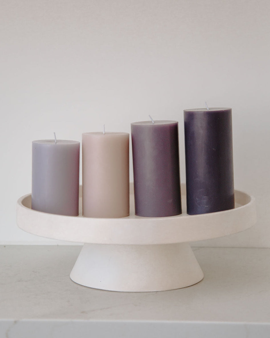 Four purple candles on a white cake stand against a light gray background