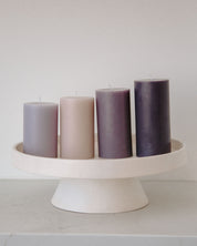 Four purple candles on a white cake stand against a light gray background