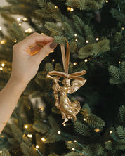 Gold angel ornament being hung on a decorated Christmas tree with lights.