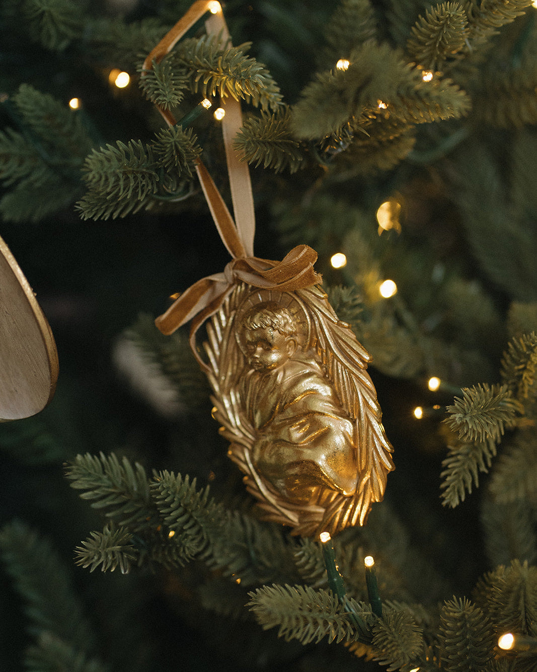 Gold angel Christmas ornament on a decorated tree with lights.