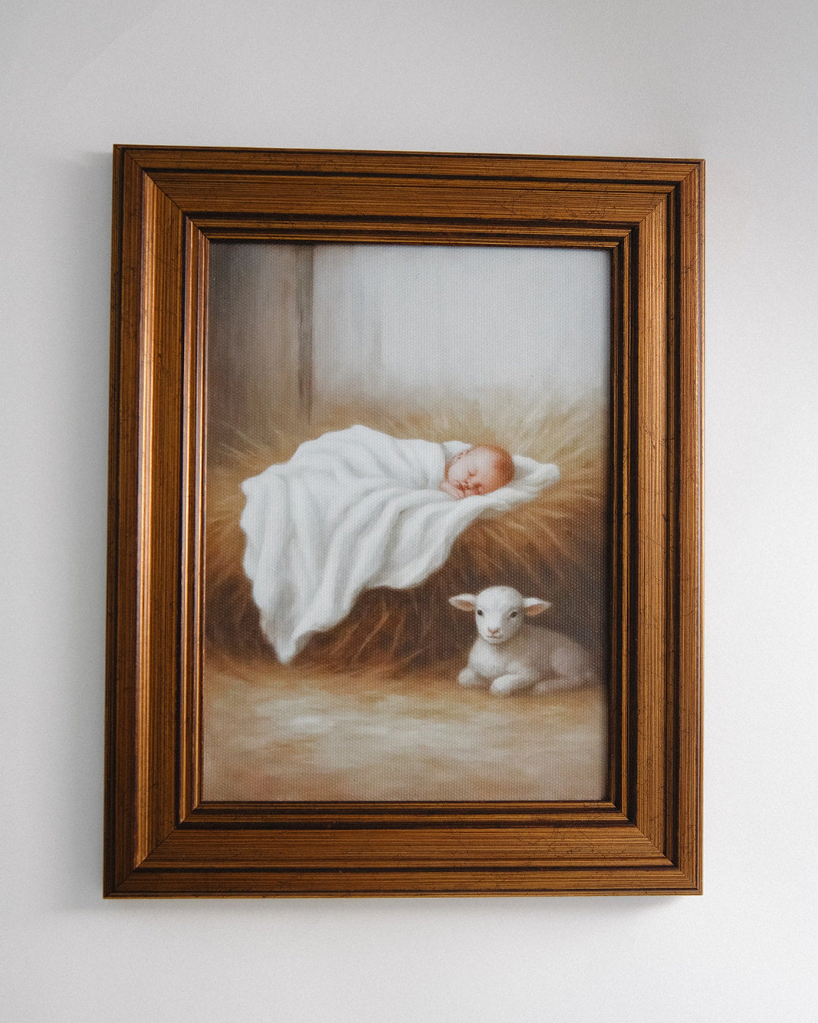Framed artwork of a baby in a manger with a lamb on a white wall