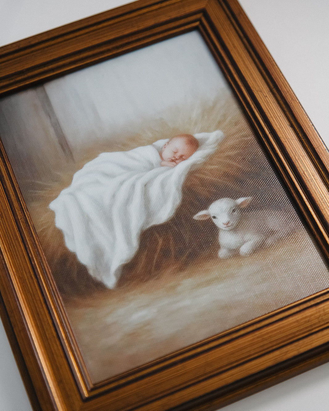 Framed artwork of a baby wrapped in a blanket next to a lamb on a textured surface.
