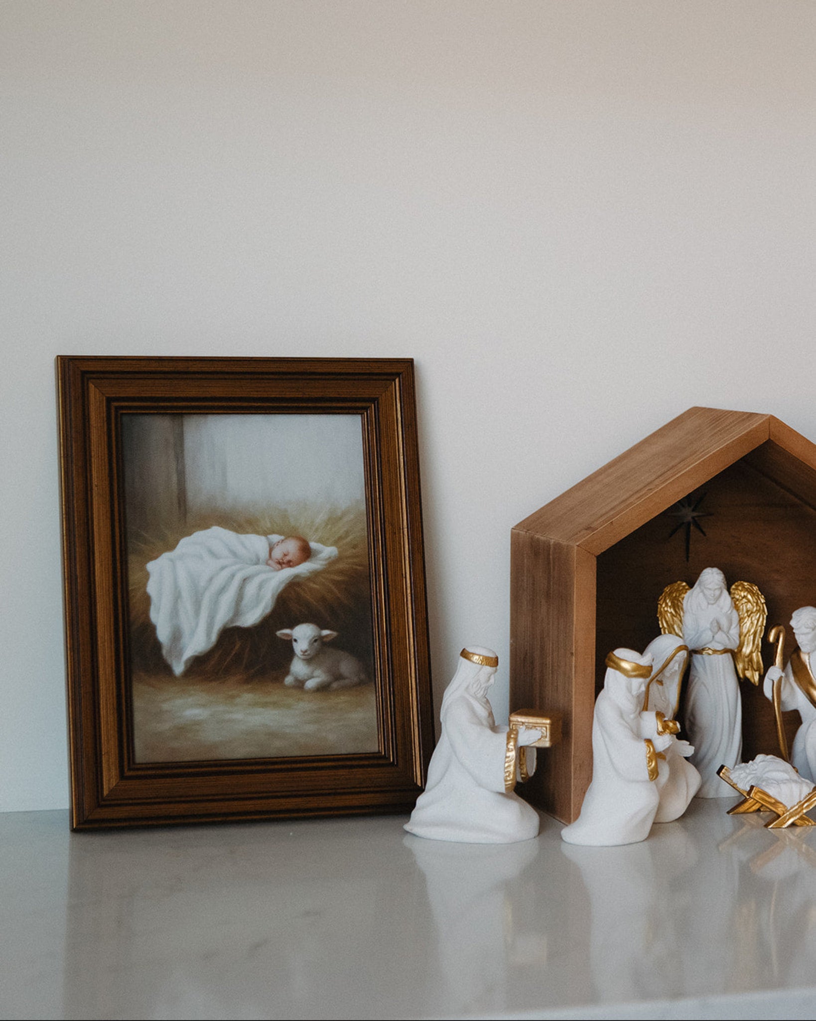 Decorative nativity scene with a framed painting of baby Jesus on a white surface.