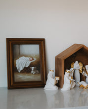Decorative nativity scene with a framed painting of baby Jesus on a white surface.