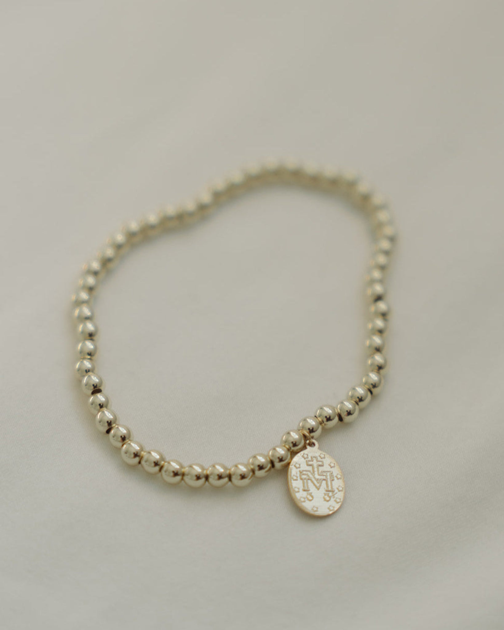 Gold Miraculous Medal beaded bracelet light gray background