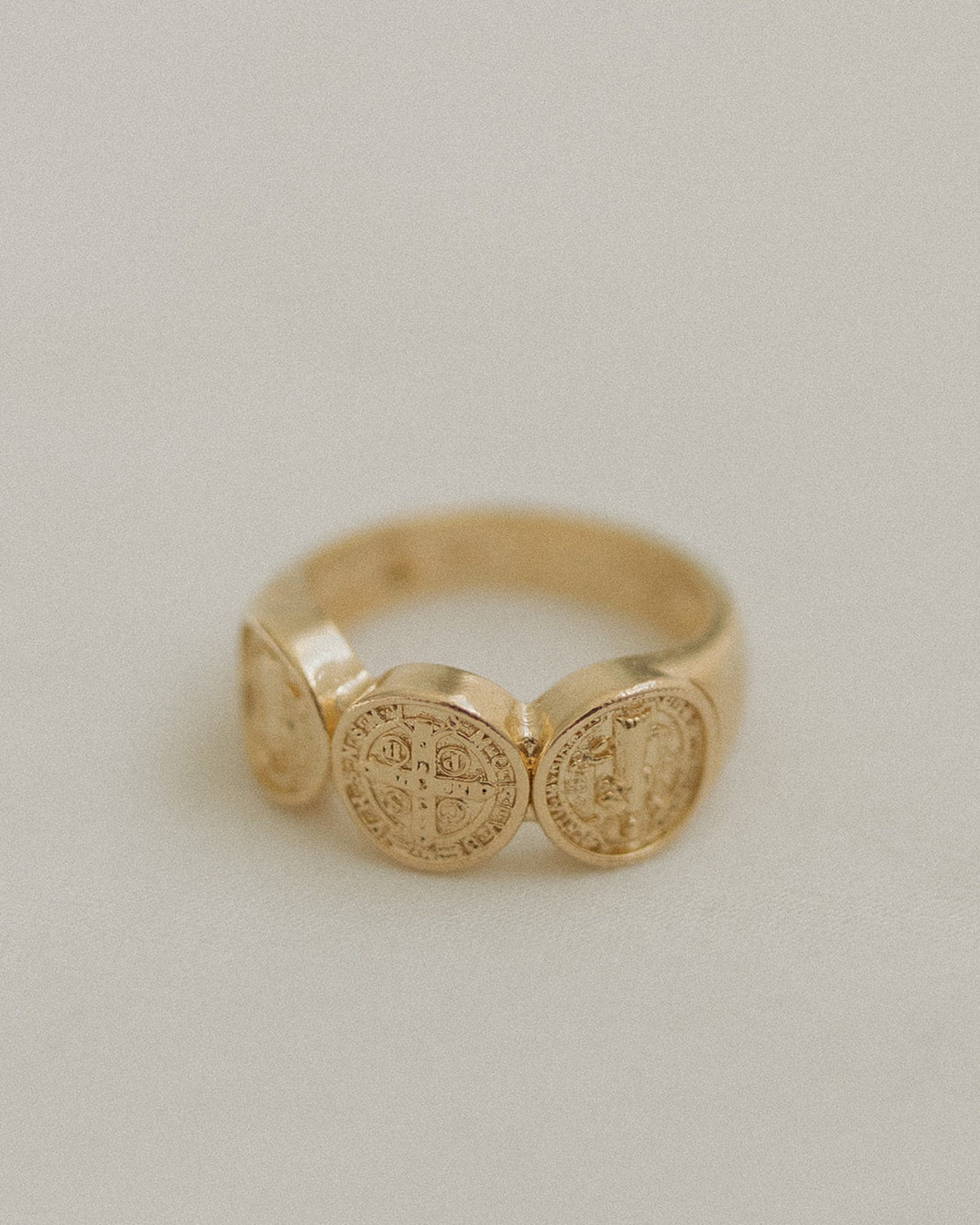 Gold ring with St. Benedict Medal on a light gray background