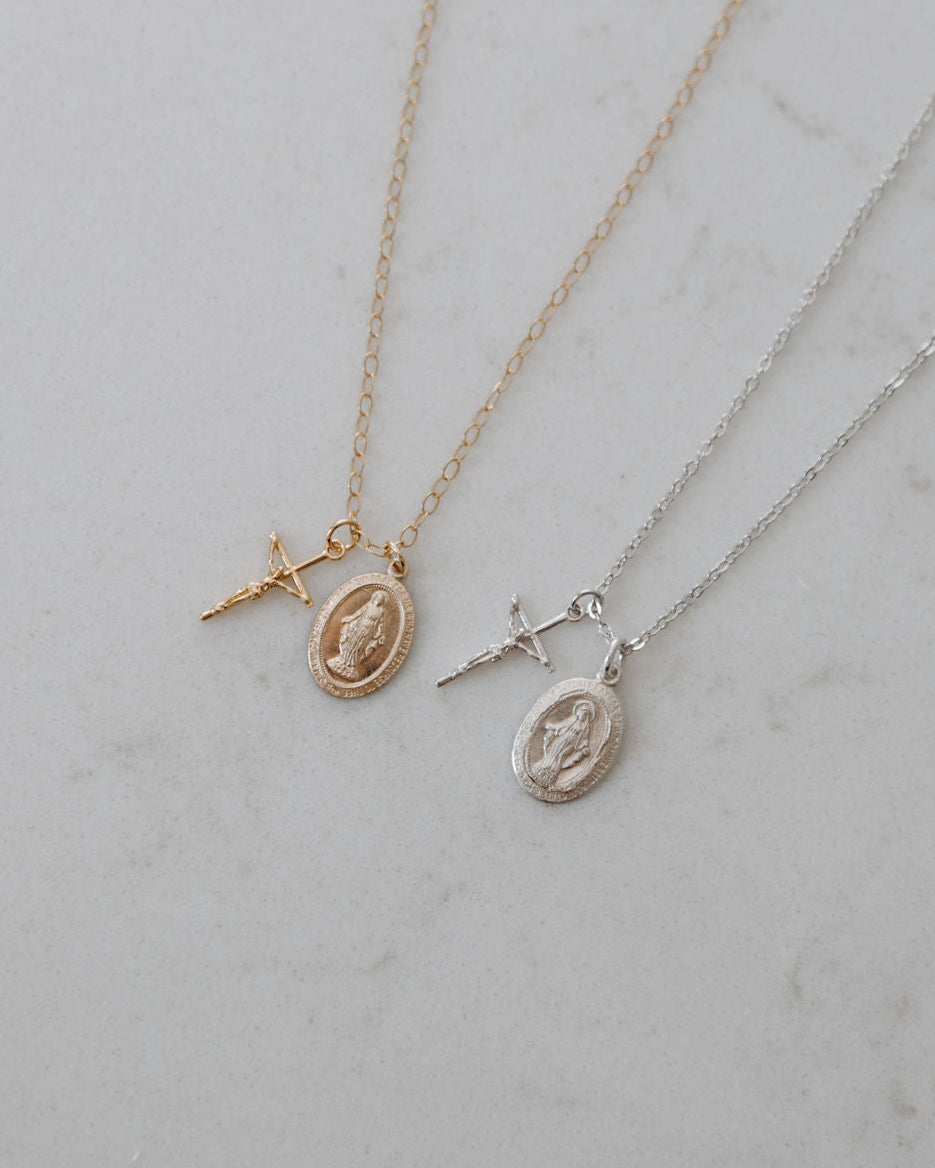 Two gold blessings necklaces with crucifix and miraculous medal pendants on a light gray background