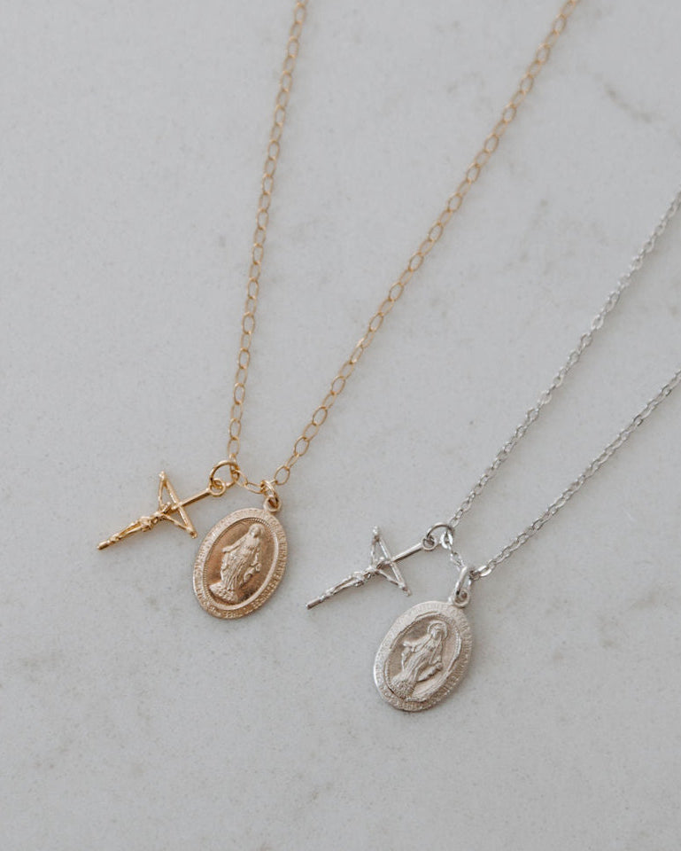 Two gold blessings necklaces with crucifix and miraculous medal pendants on a light gray background