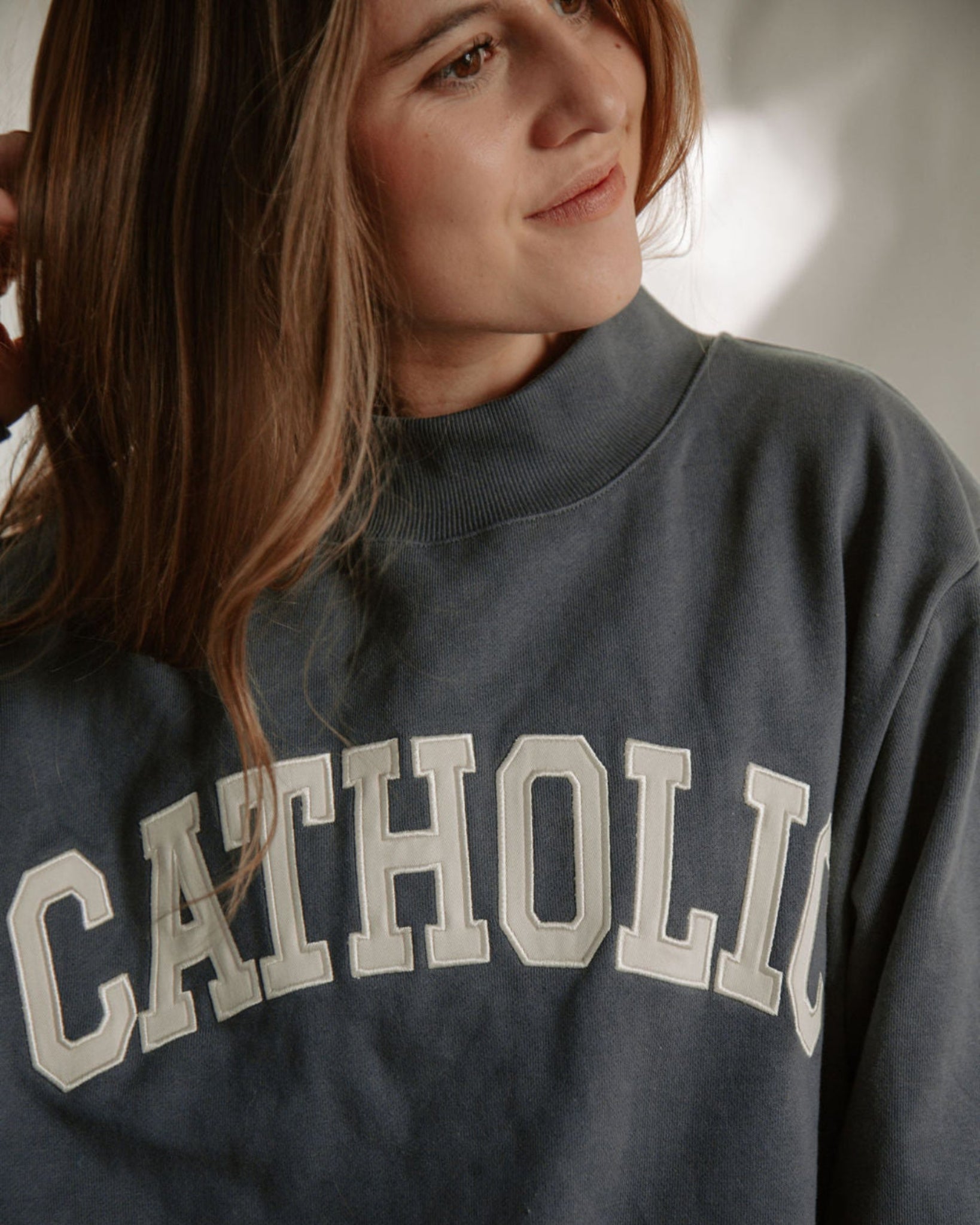 Person wearing a dark blue mock-neck varsity sweatshirt with 'CATHOLIC' printed on it.