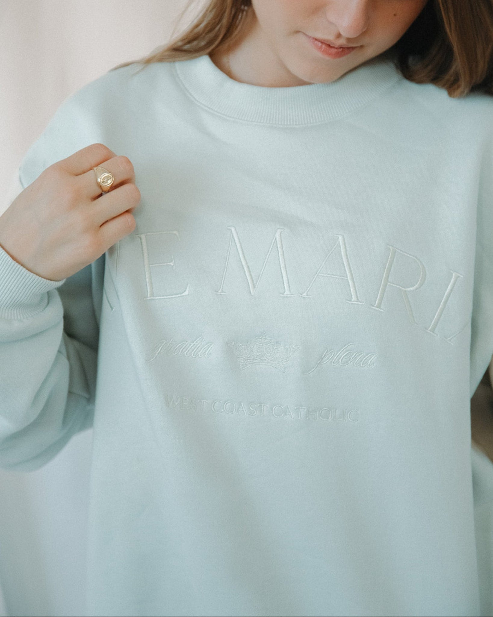 Person wearing a light blue sweatshirt with text, holding it with one hand.