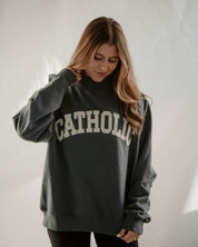 Person wearing a dark blue sweatshirt with 'Catholic' printed on it against a plain background