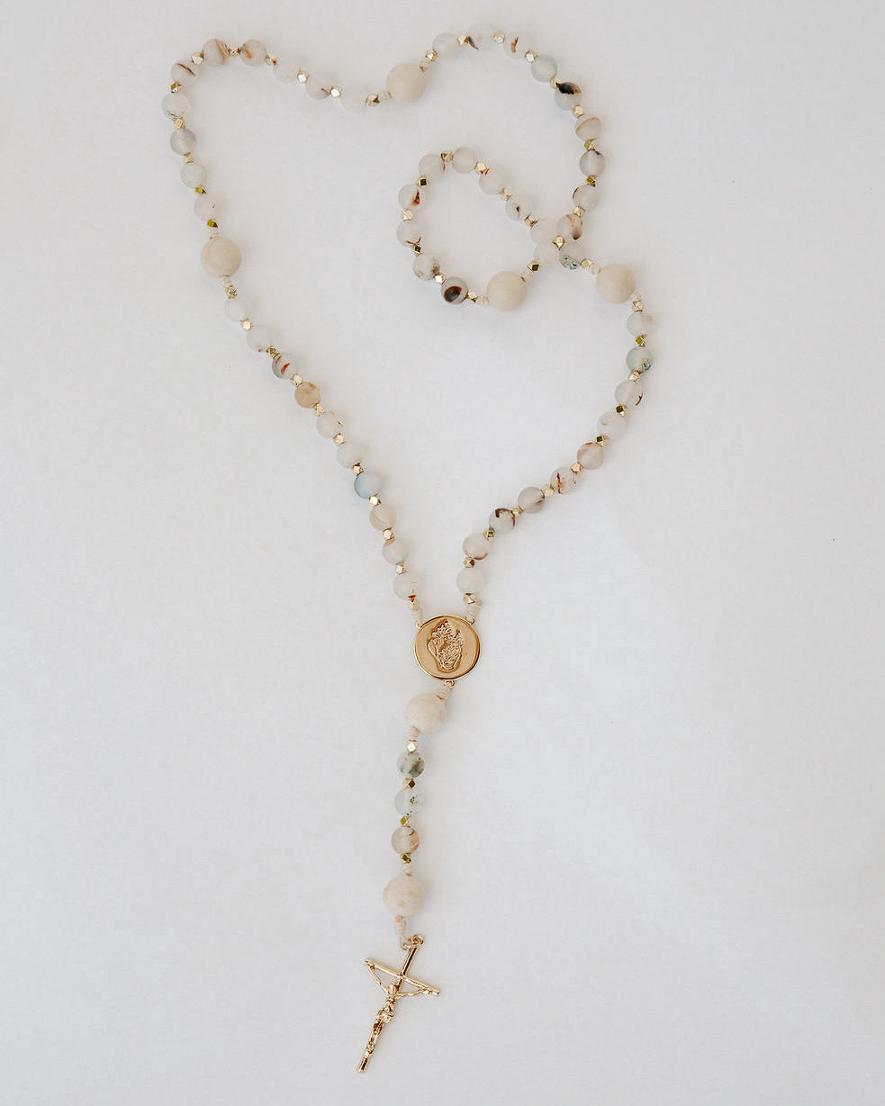 Rosary with multicolor beads and a gold cross on a light gray background