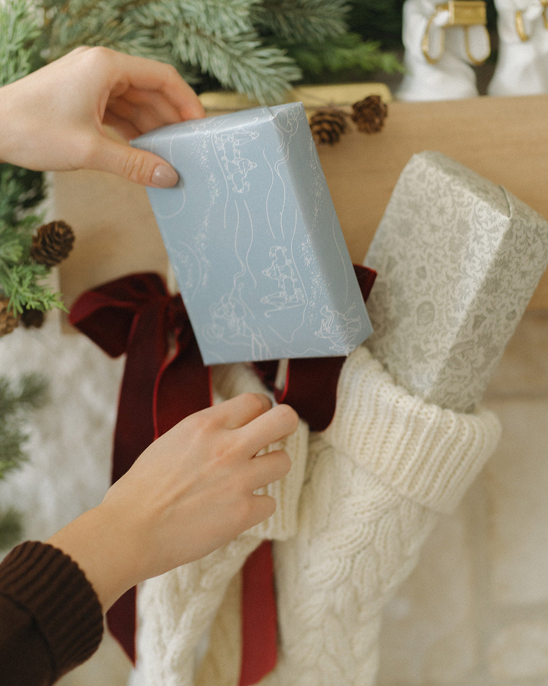 Person placing a gift next to a decorated Christmas tree with stockings.