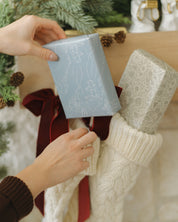 Person placing a gift next to a decorated Christmas tree with stockings.