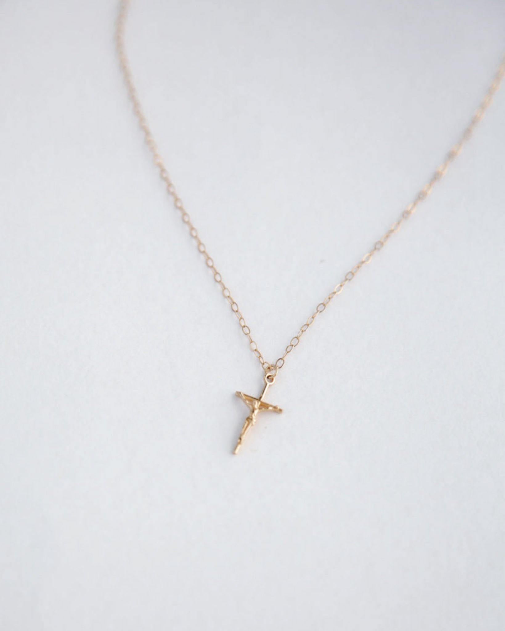 Dainty Crucifix Gold necklace on blurred white background