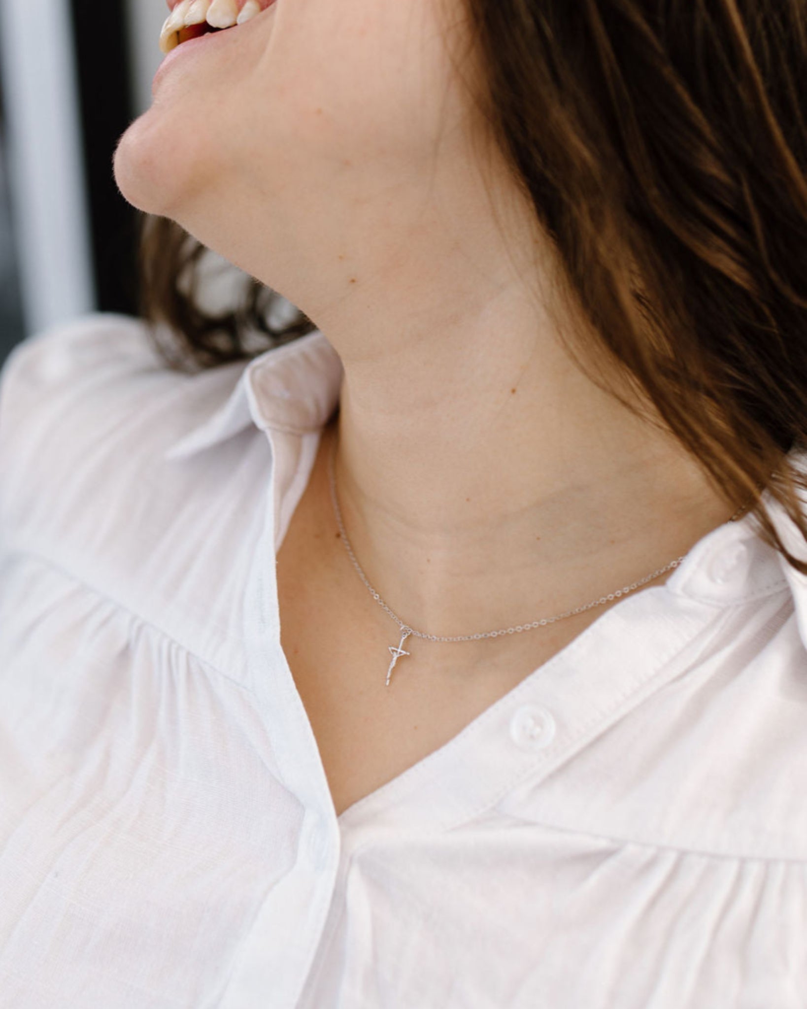 Dainty crucifix necklace silver styled on a woman's neck