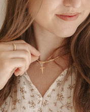 Close-up of a person wearing a gold necklace with a cross pendant.