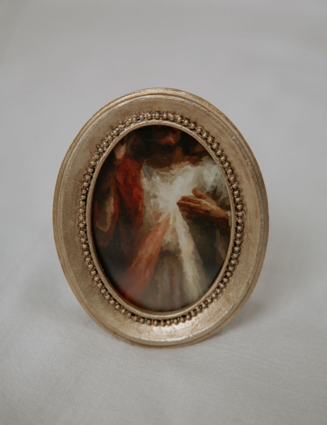 Small oval painting in a decorative gold frame with divine mercy image on a light gray background