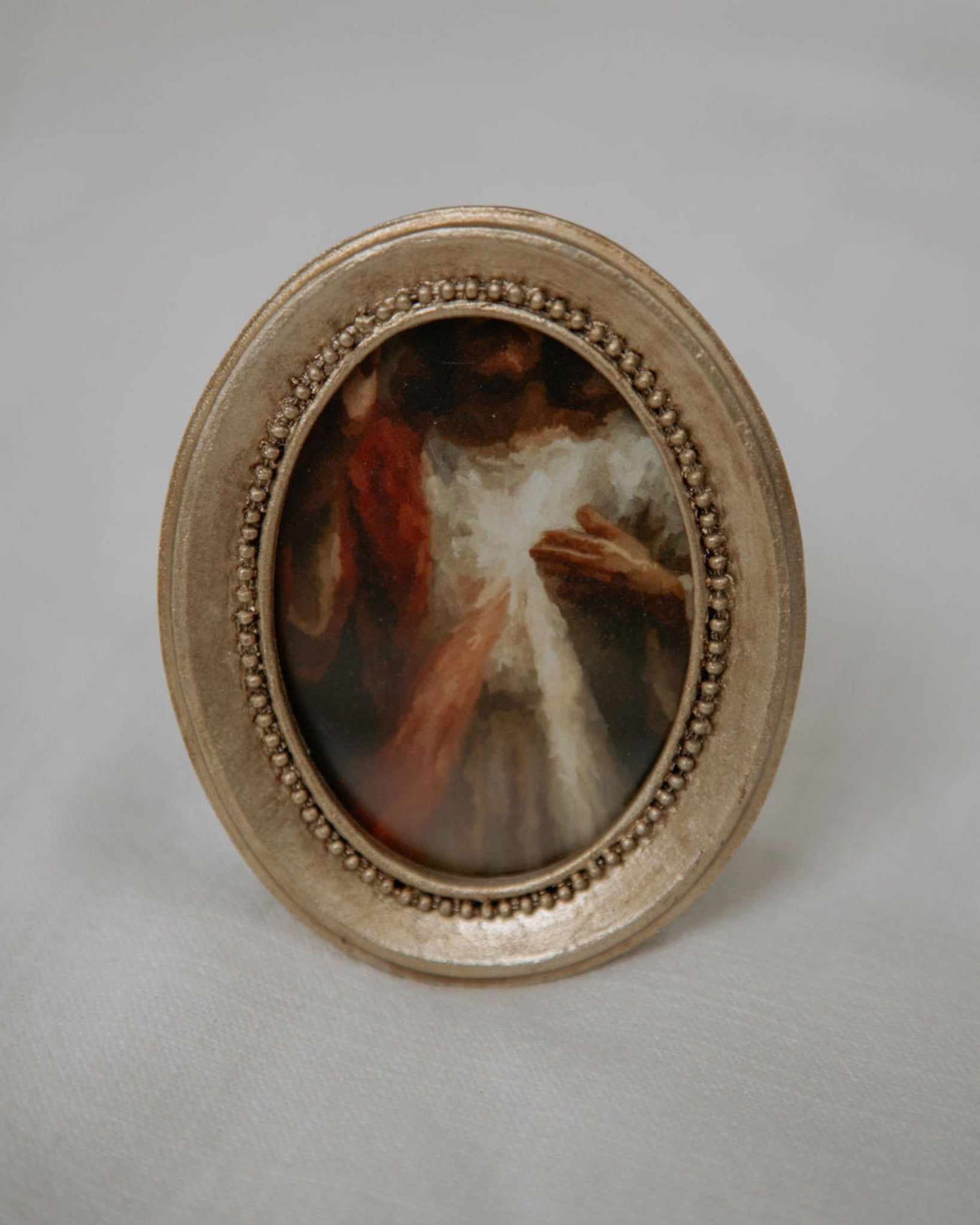 Small oval painting in a decorative gold frame with divine mercy image on a light gray background