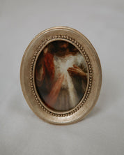 Small oval painting in a decorative gold frame with divine mercy image on a light gray background