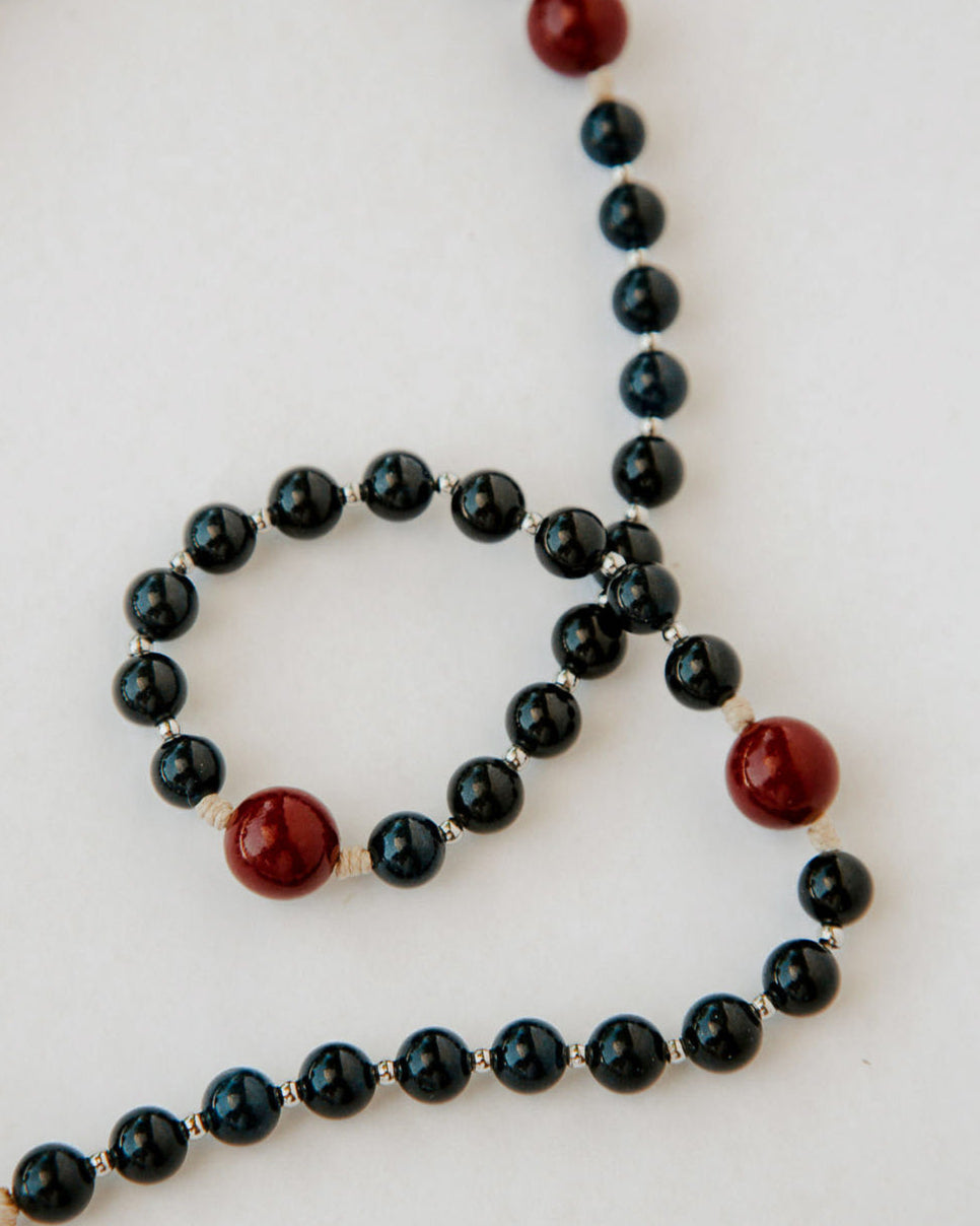 Rosary with black beads and red accents on a white background