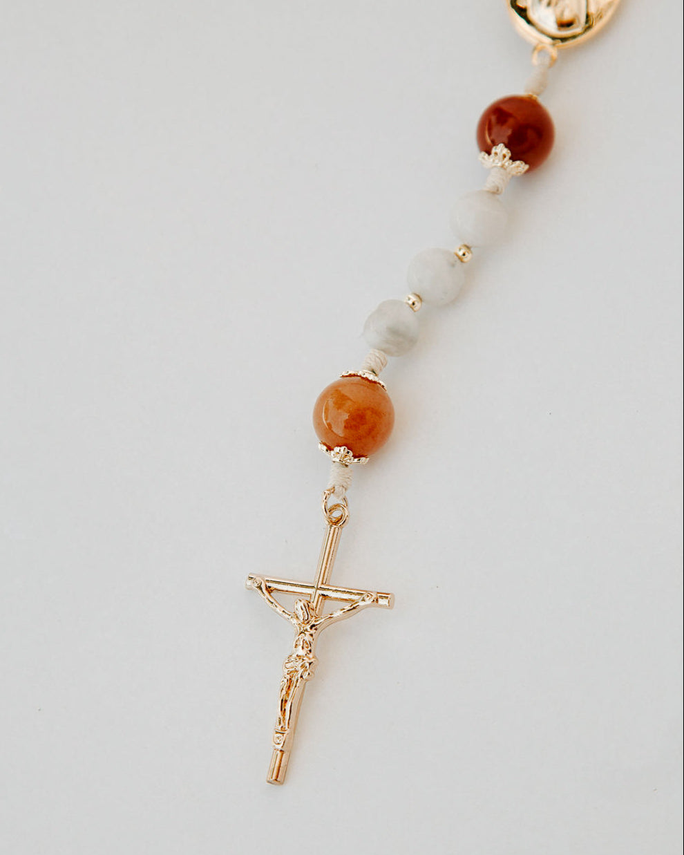Rosary with white and orange beads and gold medal details on a white background