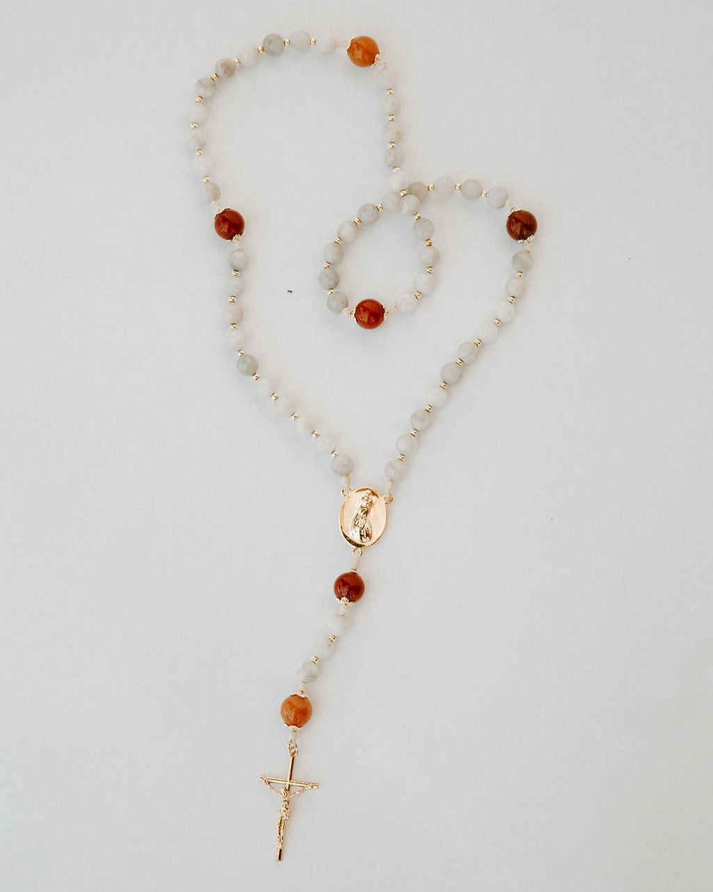 Rosary with white and orange beads and a cross on a light gray background