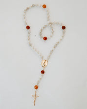 Rosary with white and orange beads and a cross on a light gray background