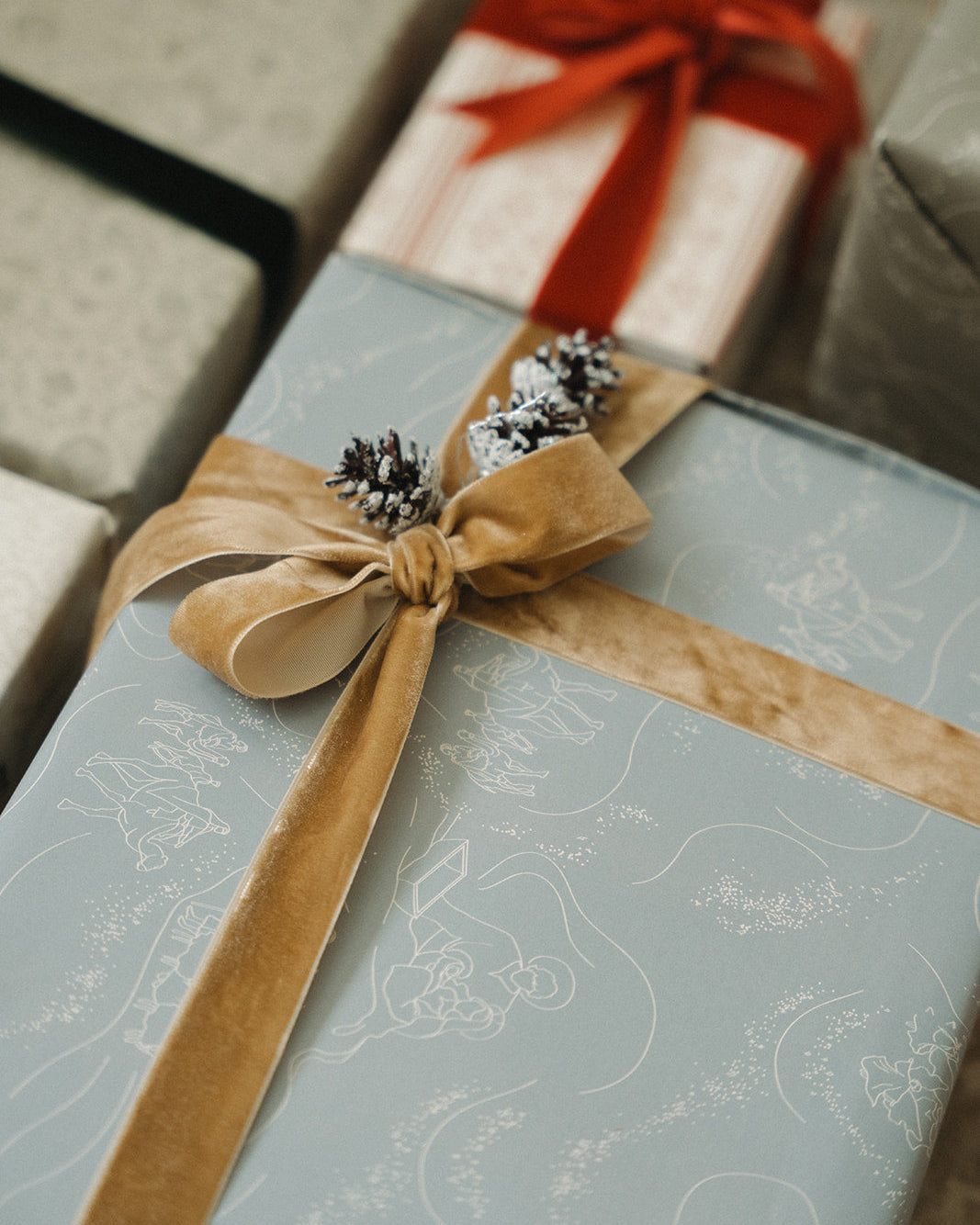 Gift wrapped in blue paper with a brown ribbon and pinecones, surrounded by other wrapped gifts.