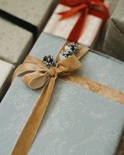 Gift wrapped in blue paper with a brown ribbon and pinecones, surrounded by other wrapped gifts.