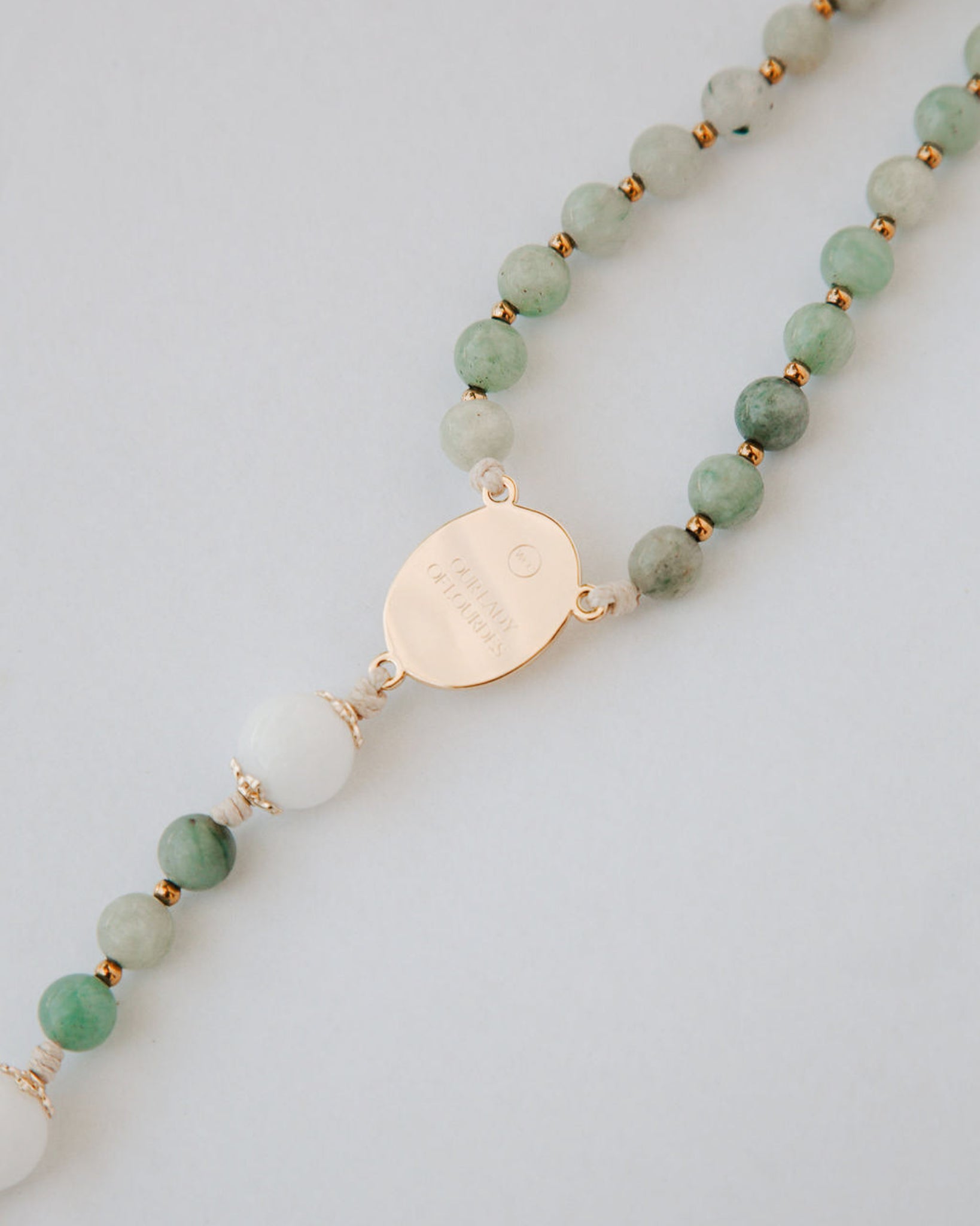 Gemstone rosary with green beads and a gold pendant on a light gray background