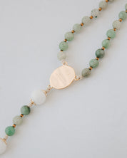 Gemstone rosary with green beads and a gold pendant on a light gray background