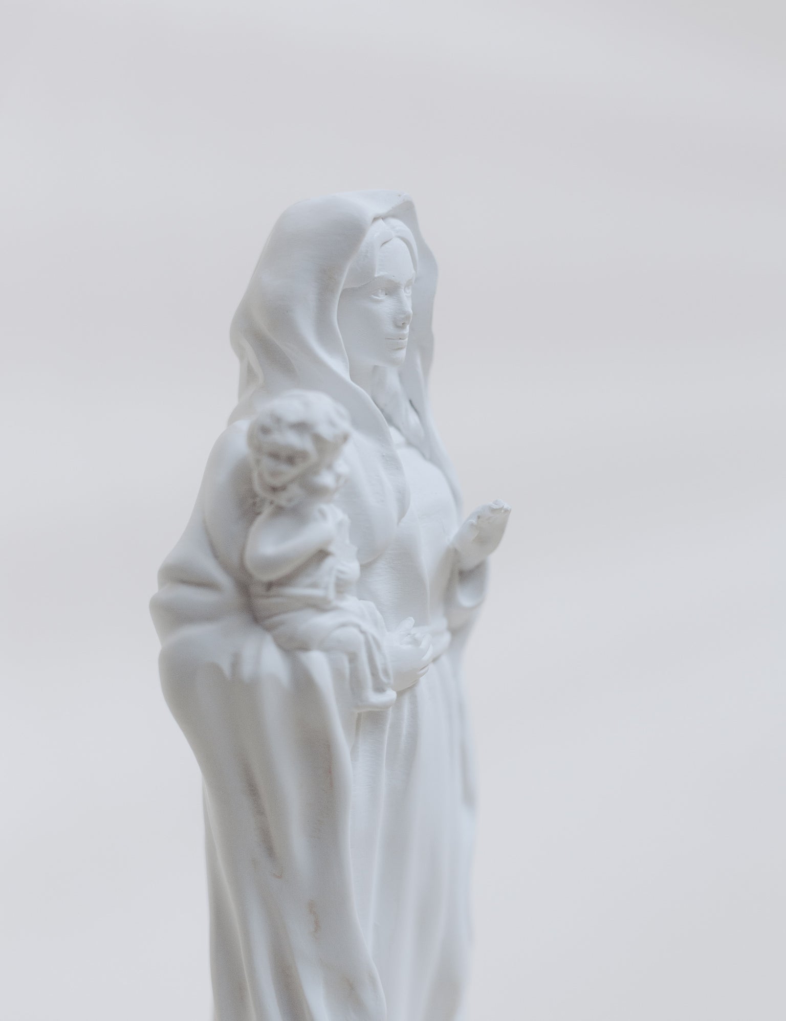 White statue of a woman holding a child against a light gray background