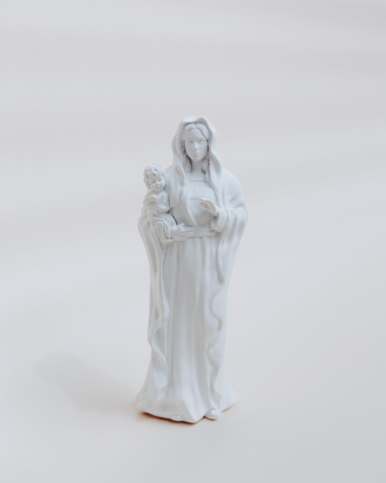 White statue of mary holding jesus on a light gray background