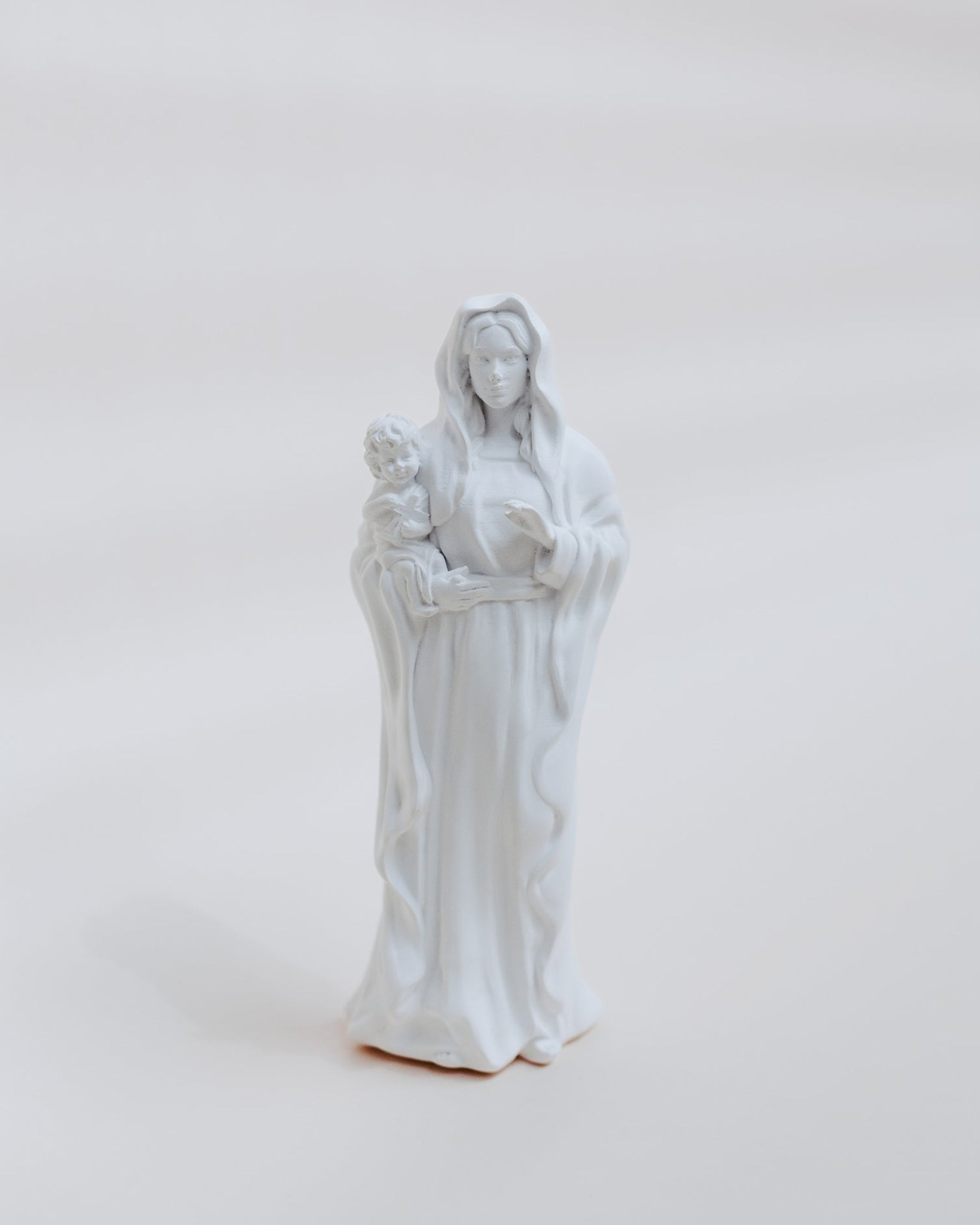 White statue of mary holding jesus on a light gray background